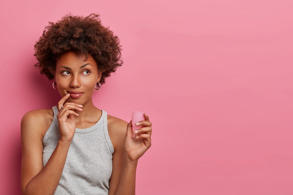 Pensive African American Woman Holds Effective Safe Affordable Menstrual Product Good Protection From Leakage Chooses Reusable Menstrual Cup Thinks How Use It Blank Empty Space Pink Wall